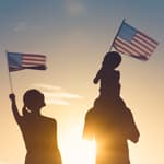 two silhoutted figures raise the American flag